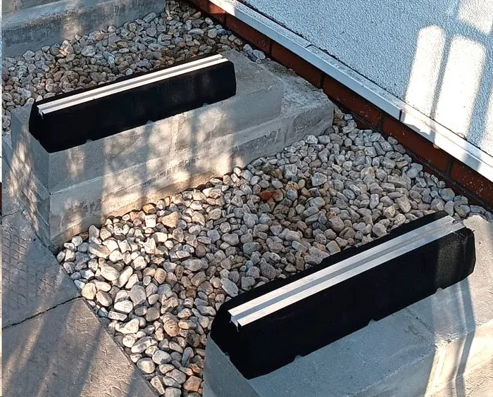 Bitumiczne podstawy pod jednostkę zewnętrzną pompy ciepła ustawione na betonowym fundamencie wysypanym żwirem